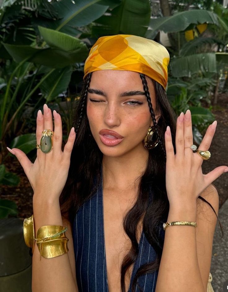 A model wearing a sunlit yellow silk scarf as a headwrap, framed by tropical foliage.